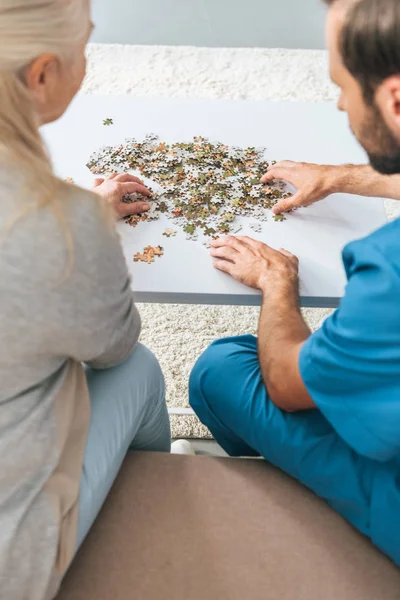 Rückansicht Einer Seniorin Und Einer Jungen Betreuerin Die Mit Puzzleteilen — kostenloses Stockfoto
