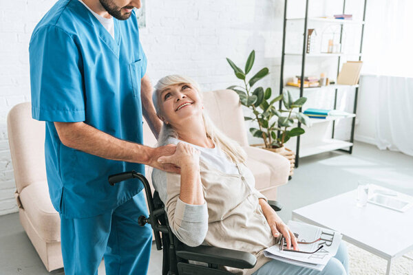 cropped shot of smiling senior woman in wheelchair looking at male caregiver