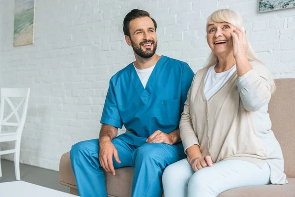 Lächelnde Junge Sozialarbeiterin Blickt Fröhliche Seniorin Die Smartphone Spricht — Stockfoto