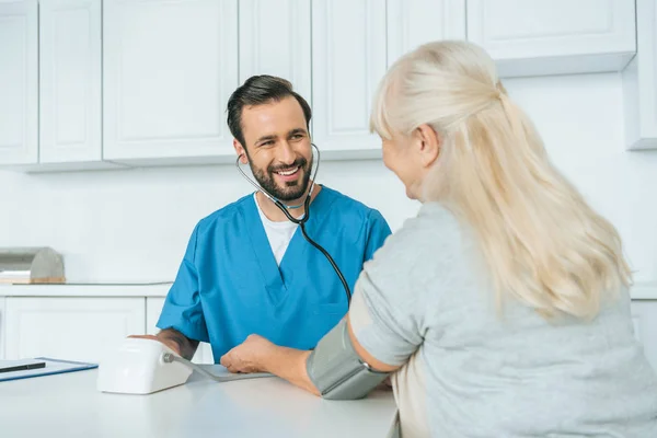 年配の女性に血圧測定のオスの看護婦の笑顔 — ストック写真