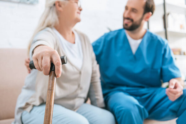 close-up view of senior woman holding walking cane and looking at smiling male nurse 