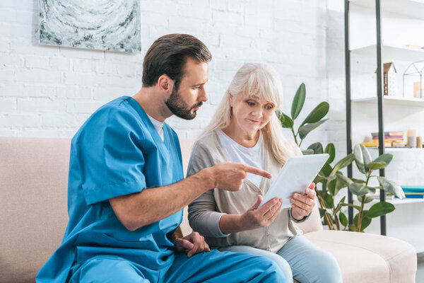 young social worker looking at senior woman using digital tablet