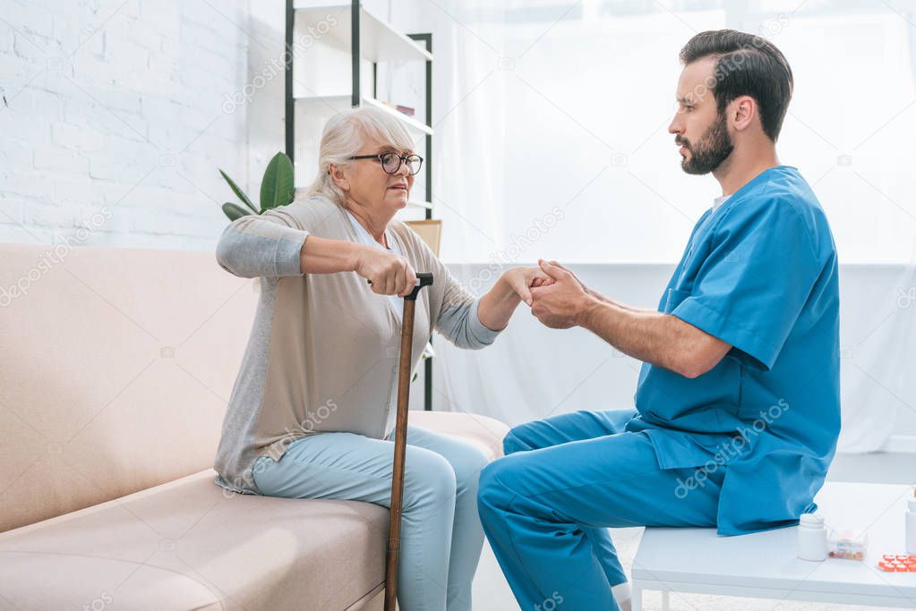 side view of male nurse helping senior woman with walking stick