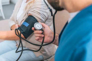 close-up partial view of caregiver measuring blood pressure to senior woman  clipart