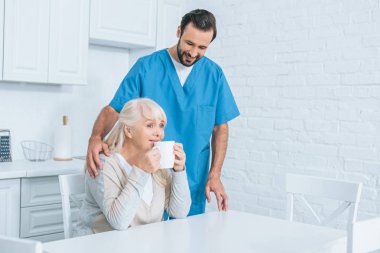 Erkek sosyal görevli üst düzey kadın mutfakta çay içme bakarak gülen 
