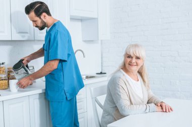 oturma ve mutfak sıcak içecek dökülen caregiver süre kamera gülümseyen mutlu kadın kıdemli