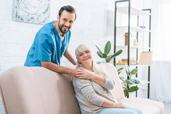 счастливая пожилая женщина и молодой социальный работник улыбаются в камеру вместе
