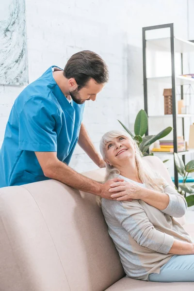 Lächelnde Seniorin Sitzt Auf Couch Und Schaut Junge Sozialarbeiterin — Stockfoto