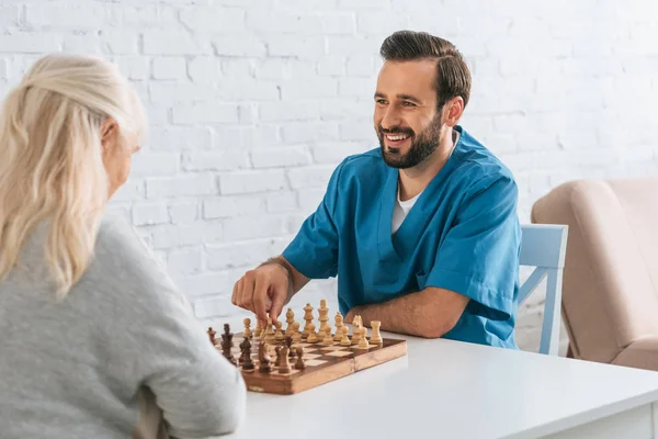 Usměvavý Mladý Muž Hraje Šachy Starší Žena Péče Seniory Koncept — Stock fotografie