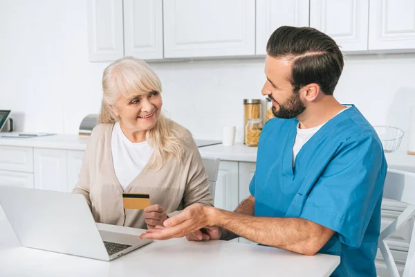 Lachende Jonge Verzorger Zoek Naar Senior Vrouw Creditcard Bedrijf Met — Stockfoto