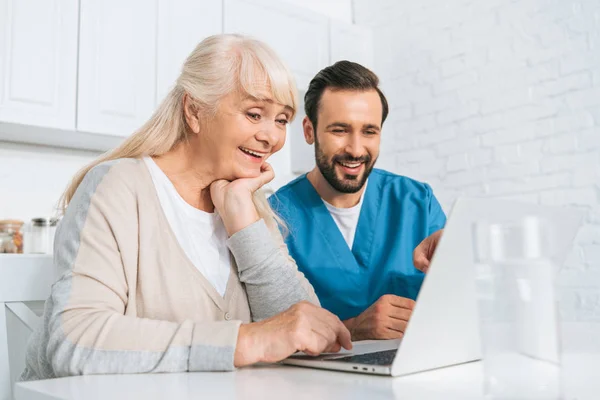 Lächelnde Junge Betreuerin Und Glückliche Seniorin Benutzen Gemeinsam Laptop — Stockfoto