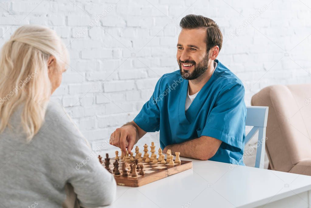 smiling young man playing chess with senior woman, elderly care concept
