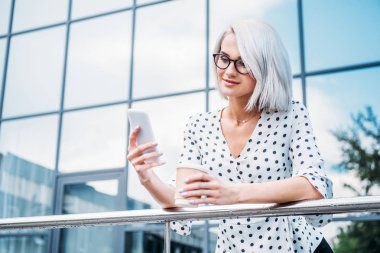 işkadını kahve ile gözlük içinde Smartphone sokakta kullanmaya devam