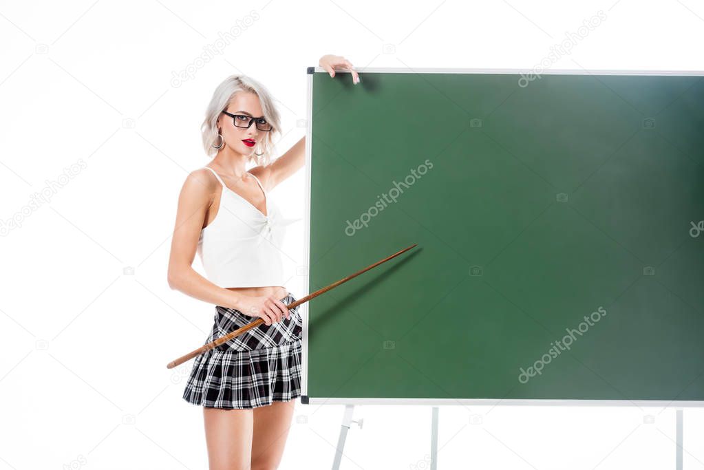 young sexy woman in school skirt pointing at empty chalkboard with pointer isolated on white