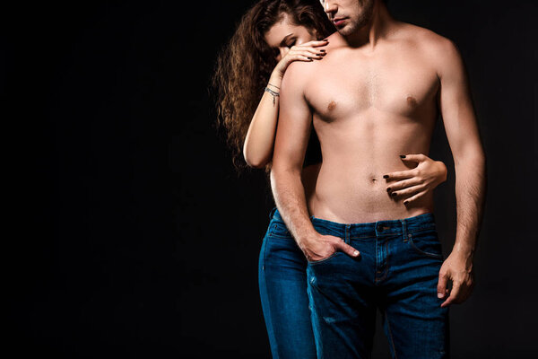 partial view of woman hugging shirtless boyfriend in jeans isolated on black