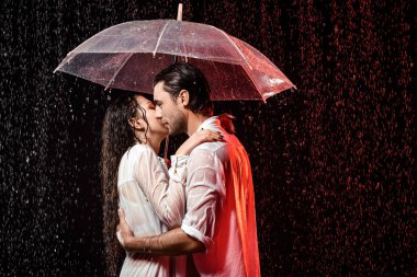 side view of romantic couple in white shirts with umbrella standing under rain on black backdrop clipart