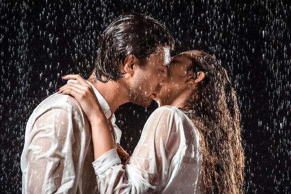 side view of couple kissing under rain isolated on black