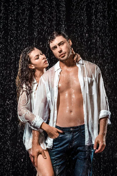 portrait of sexy couple in white shirts standing under rain isolated on black