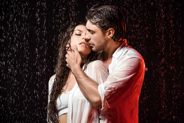 portrait of sexy couple in white shirts standing under rain on black backdrop