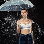 Portrait of pensive woman with umbrella swilled with water isolated on black