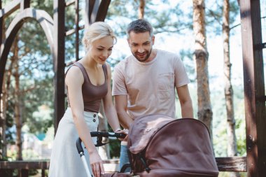 parents looking at baby pram in park clipart