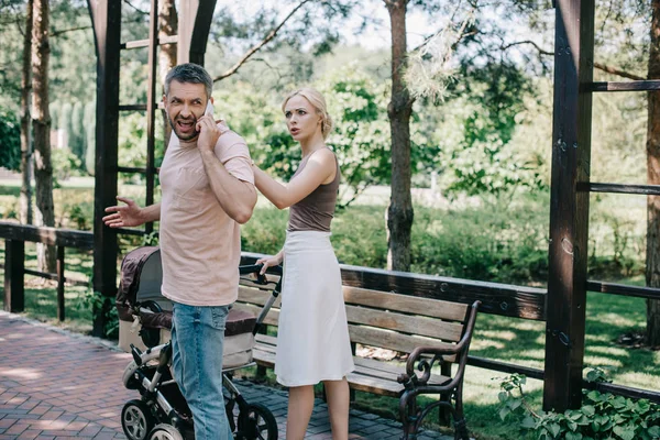 Father Talking Smartphone Baby Carriage Park Angry Mother Touching Him — Free Stock Photo