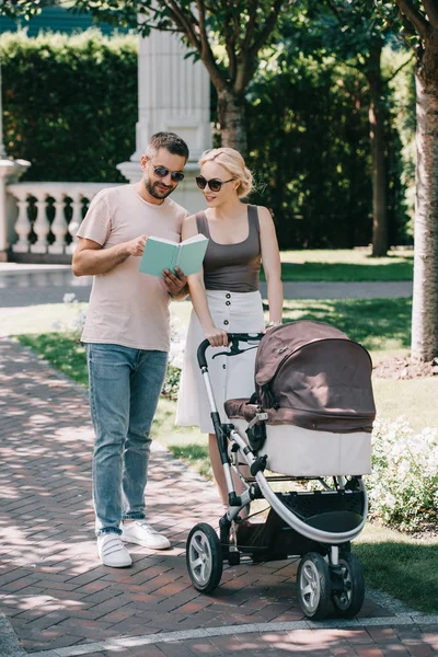 Parents Standing Baby Carriage Park Looking Book — Free Stock Photo