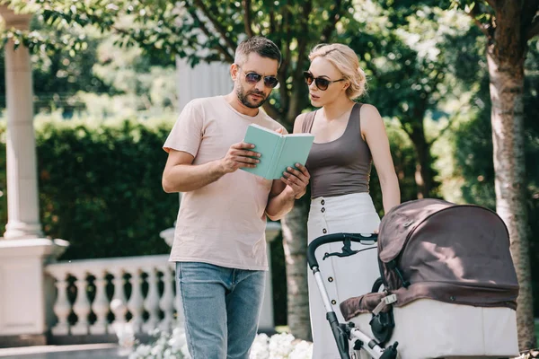 Parents Standing Baby Carriage Park Reading Book — Stock Photo, Image
