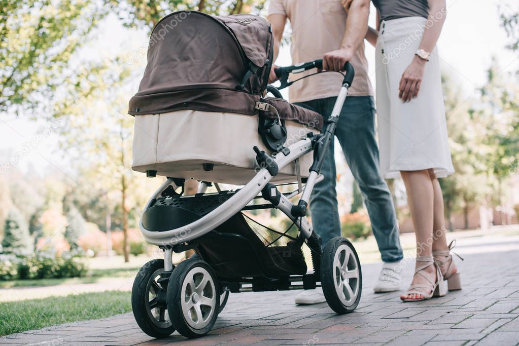 cropped image of mother and father walking with baby carriage in park