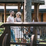 Side view of happy parents with baby carriage on bridge in park