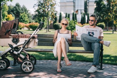 Bebek arabasını park yakınındaki bankta oturmuş ve dergi ve gazete okuma ebeveynler