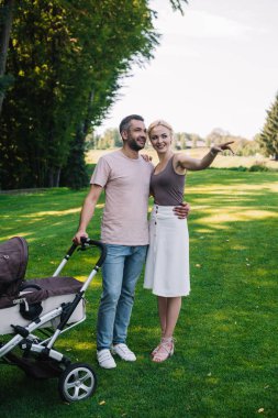 Bebek arabası Park yakınındaki koca için bir şeye işaret eden karısı