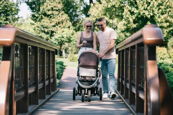 Sonrientes Padres Caminando Con Carro Bebé Puente Parque — Foto de Stock