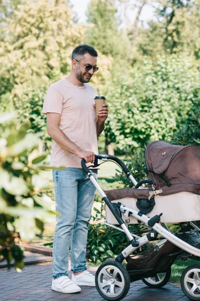 Πατέρας Περπατώντας Μωρό Μεταφορά Στο Πάρκο Και Κρατώντας Φλιτζάνι Καφέ — Φωτογραφία Αρχείου