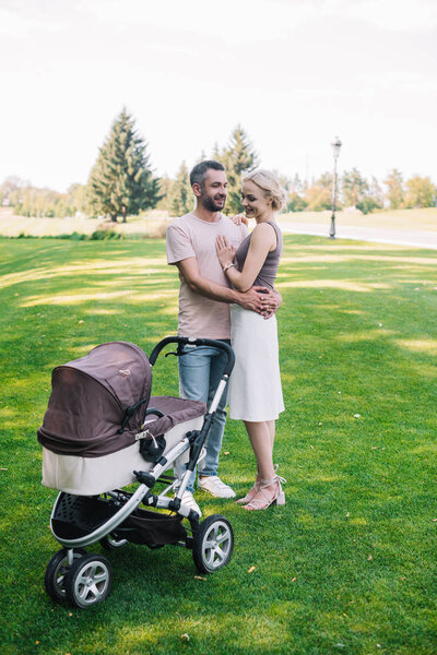 parents cuddling near baby carriage in park