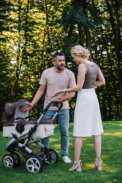 angry parents quarreling near baby carriage in park