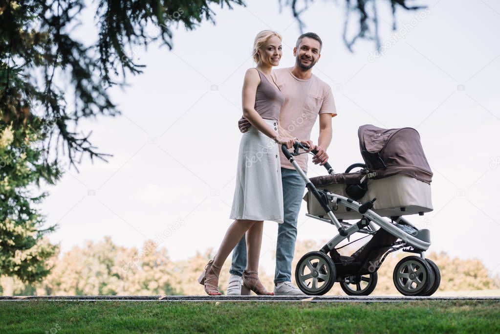 happy parents walking with baby carriage in park