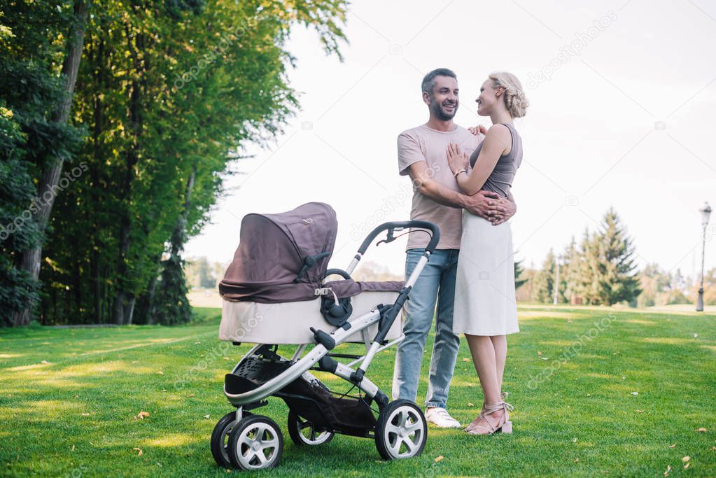 parents hugging near baby carriage in park