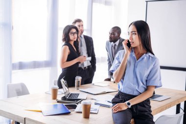 Asya işkadını smartphone ve Office arkasında meslektaşları konuşurken seçici odak