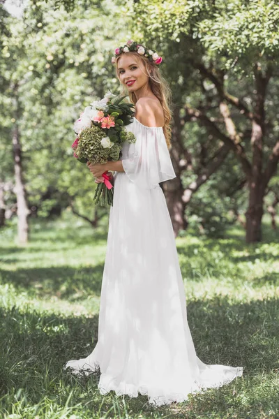 花の花束を持って 屋外でカメラで笑顔のウェディング ドレスで美しい若い花嫁 — ストック写真