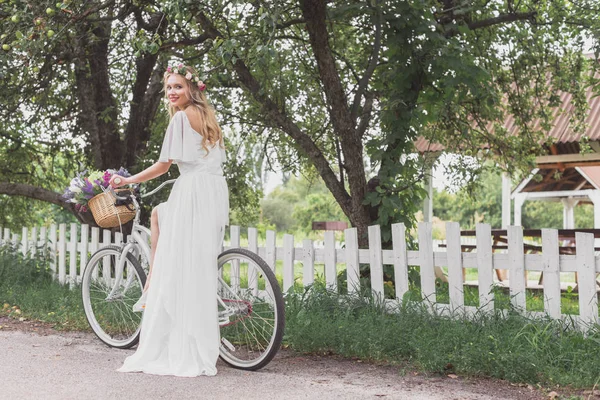 自転車に乗って カメラで笑顔のウェディング ドレスで美しい若い花嫁 — ストック写真