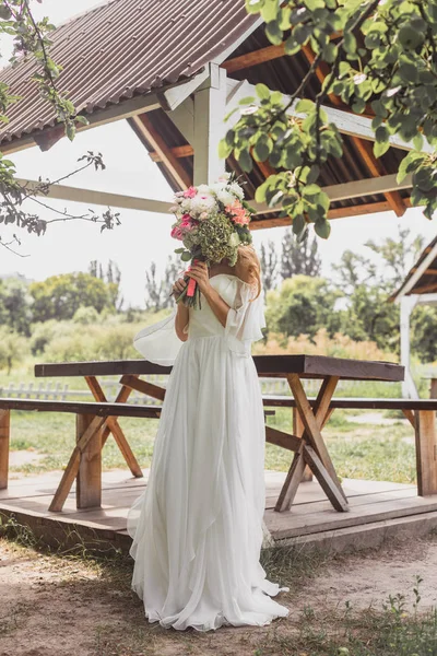 屋外の花の花束で顔を隠す若い花嫁  — 無料ストックフォト