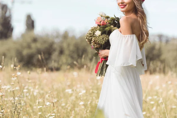 屋外の結婚式のブーケを保持している白いドレスの若い花嫁の笑顔のクロップ撮影 — ストック写真