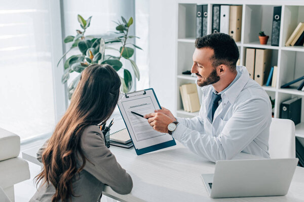 general practitioner pointing on insurance claim form to patient in clinic