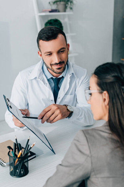 cheerful doctor pointing on insurance claim form to patient in clinic