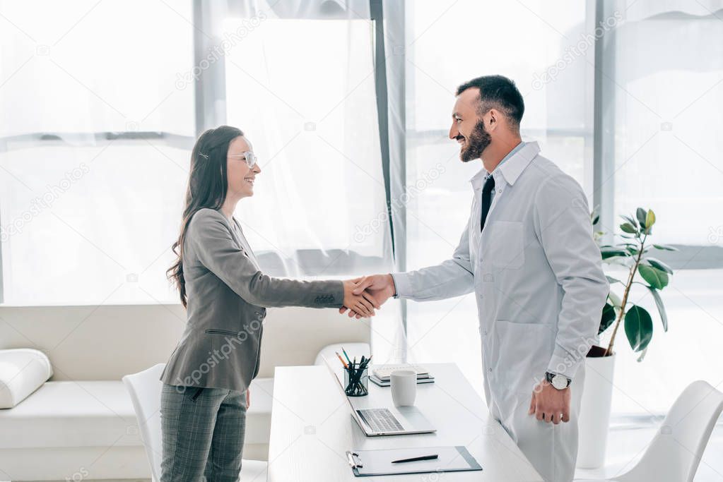 side view of smiling patient and doctor shaking hands in clinic