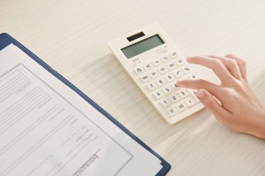 cropped view of woman counting finances on calculator at table with insurance claim form clipart