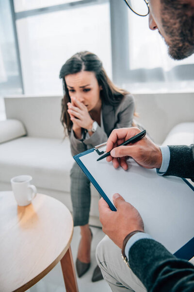 cropped image of psychologist taking notes and sad patient looking down in doctors office