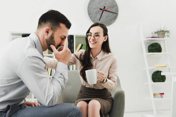 smiling psychologist giving cup of tea to upset patient in office