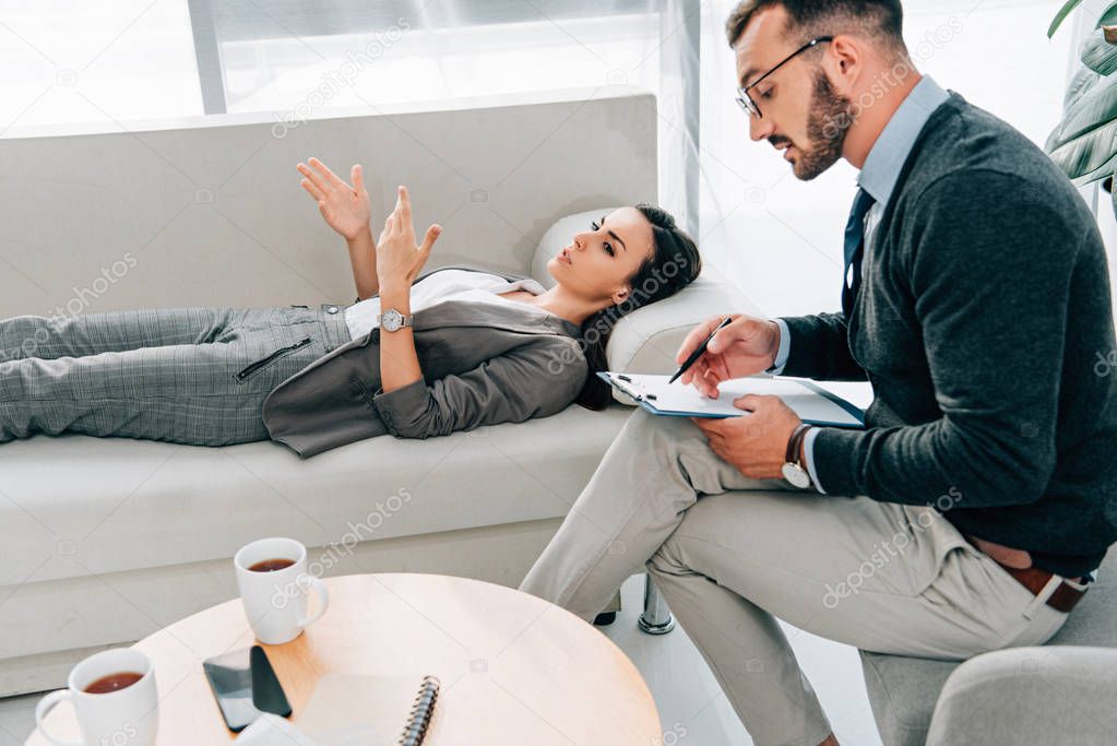 female patient lying on sofa and talking with psychologist in office